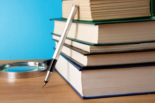 Pilha de livro, lupa e caneta sobre madeira — Fotografia de Stock