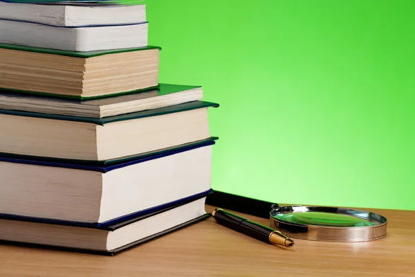 Stapel Bücher, Stift und Lupe auf dem Tisch — Stockfoto