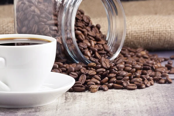 Kopje van koffie en glazen pot vol bonen op zak — Stockfoto