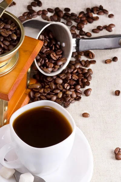Xícara de café, panela cheia de grãos e moedor no saco — Fotografia de Stock