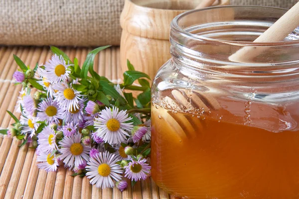 Honey, flowers and pot on straw table — Stock Photo, Image