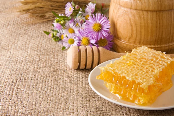 Honeycomb, flowers and honey in pot on sack — Stock Photo, Image