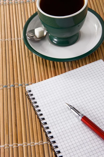 Xícara de café e caneta de tinta com caderno verificado na palha — Fotografia de Stock