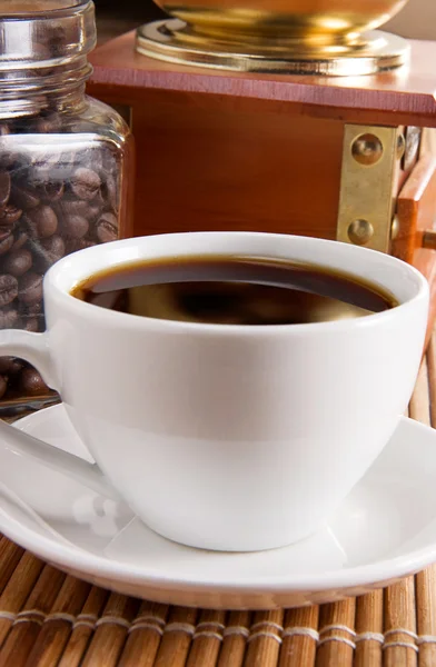 Xícara de café, panela cheia de grãos e moedor na mesa — Fotografia de Stock