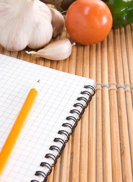 Caderno, alho e tomate com lápis na cozinha — Fotografia de Stock