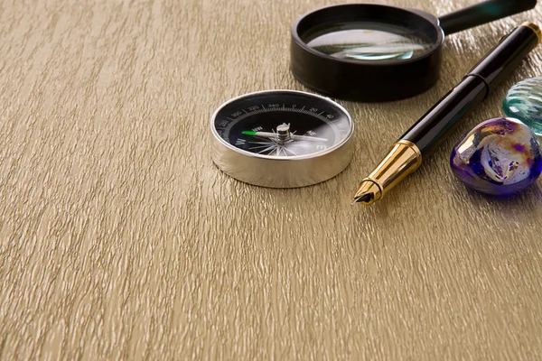 Bussola, penna inchiostro e lente d'ingrandimento su sfondo oro vecchio — Foto Stock