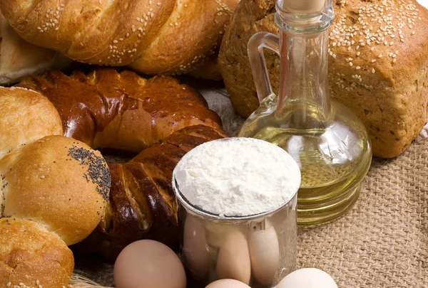 Bread, eggs, buns, flour in pot and oil on sack — Stock Photo, Image