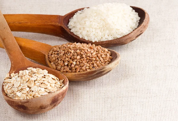 Aveia, arroz e trigo sarraceno em colher de madeira no saco — Fotografia de Stock