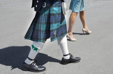 A man dressed up a Scottish kilt and a woman wearing a dress walk down the street. clipart