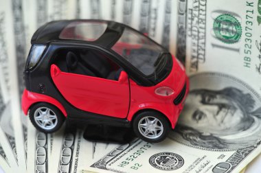 Black and red car over a lot of dollar bills isolated on white (selective focus) clipart