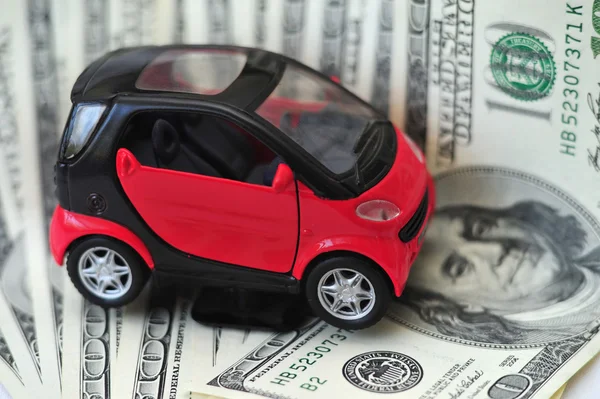 Black and red car over a lot of dollar bills isolated on white (selective focus) — Stock Photo, Image