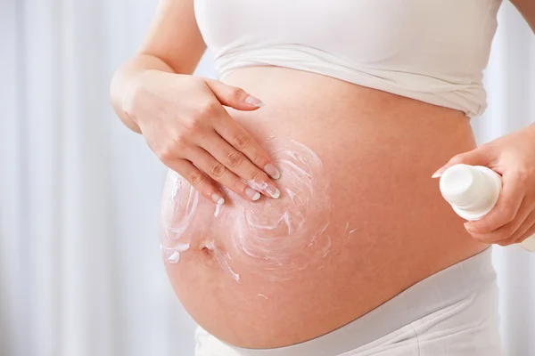 妊娠中の女性のおなかの上の保湿クリームを使用してください。 — ストック写真