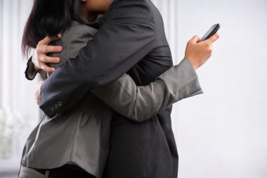 Business couple hug yet the woman still using cell phone clipart