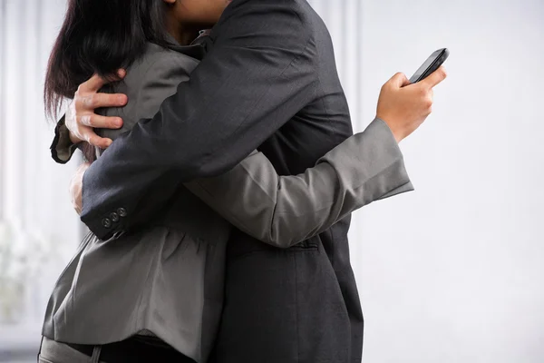 Business couple hug yet the woman still using cell phone — Stock Photo, Image