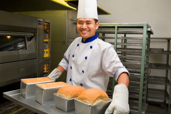 Baker holding fresh bread from oven — Stock Photo, Image