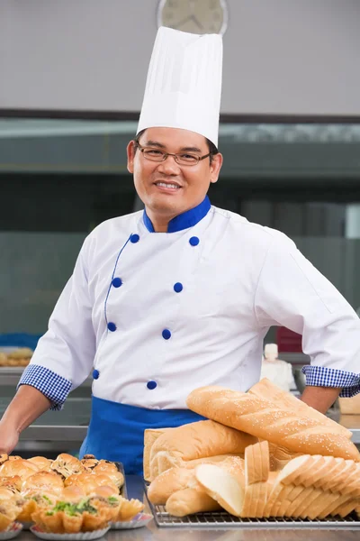 Chef ou padeiro posando na frente dos doces — Fotografia de Stock