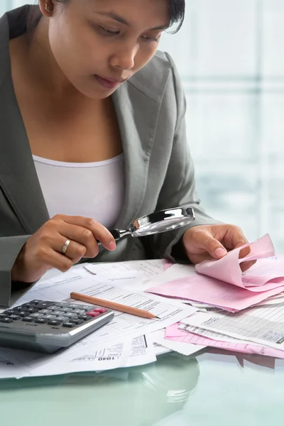 Asian businesswoman checking bills using magnifying glass — Stock Photo, Image