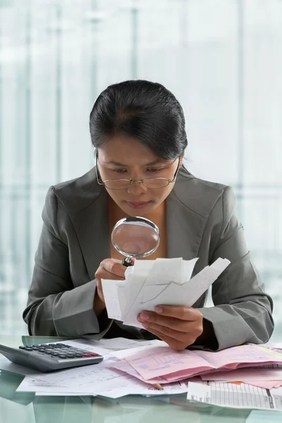 Asian businesswoman checking bills using magnifying glass — Stock Photo, Image