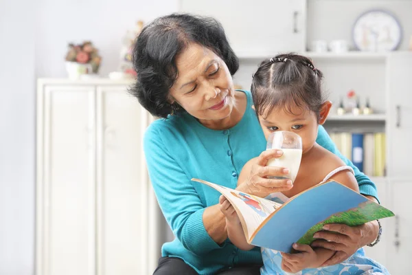 Mormor ger mjölk till hennes granddaugter — Stockfoto