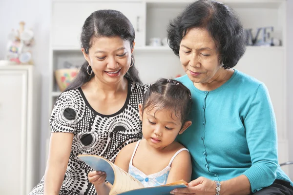 Little girl accompanied by mother and grandma reading book — Stock Photo, Image