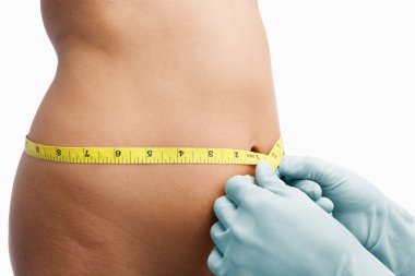 Female mid section being measure before liposuction clipart