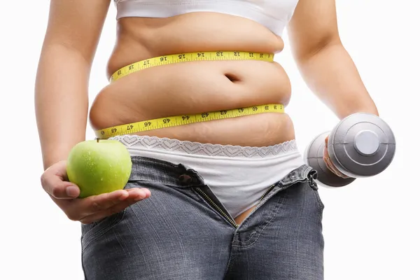 Толстая женщина в джинсах unzup держит яблоко и вес на каждой руке — стоковое фото