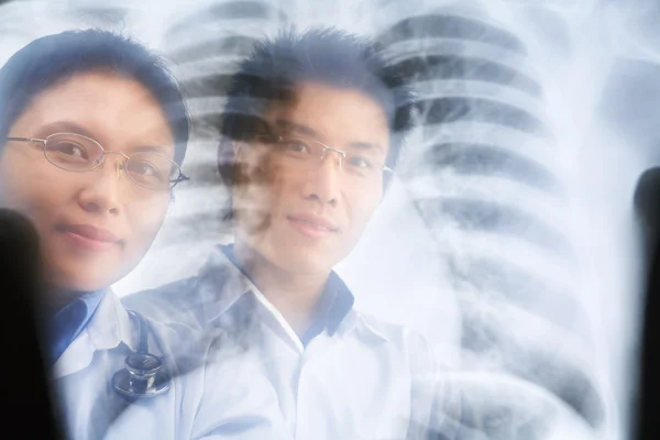 Два азиатских врача улыбаются через результат рентгена — стоковое фото