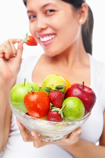Woman eating strawberry while holding bow of fruits — Stock Photo, Image