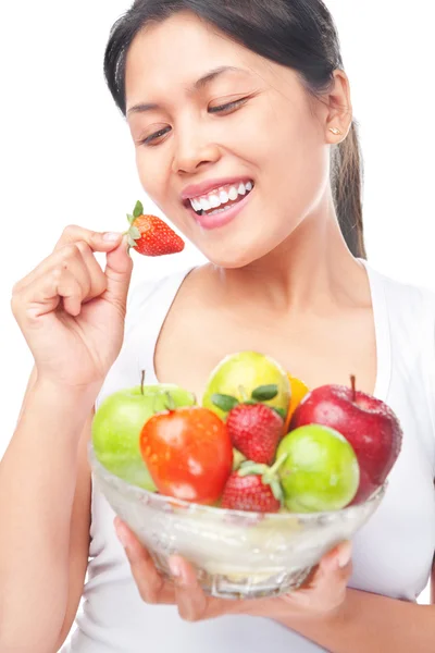 Woman eating strawberry while holding bow of fruits — Stock Photo, Image