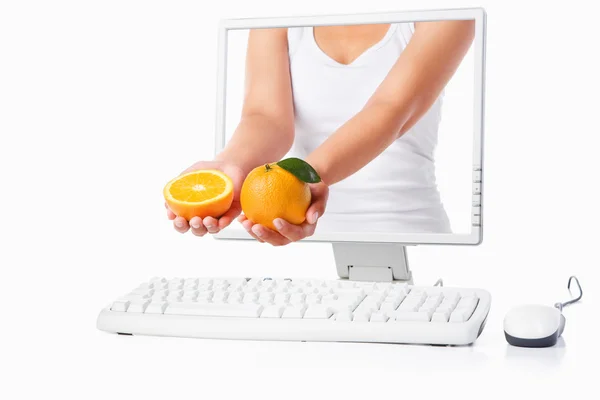 Female hand holding orange coming out from computer screen — Stock Photo, Image