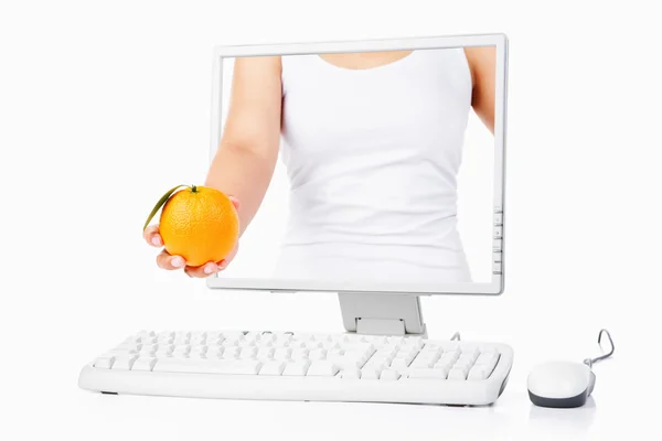 Female hand holding orange coming out from computer screen — Stock Photo, Image