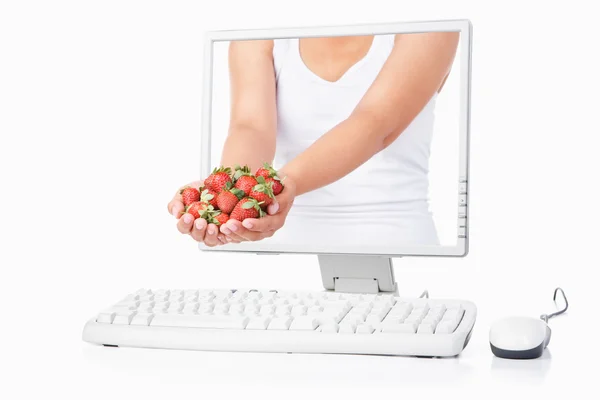 Mão feminina segurando morango saindo da tela do computador — Fotografia de Stock