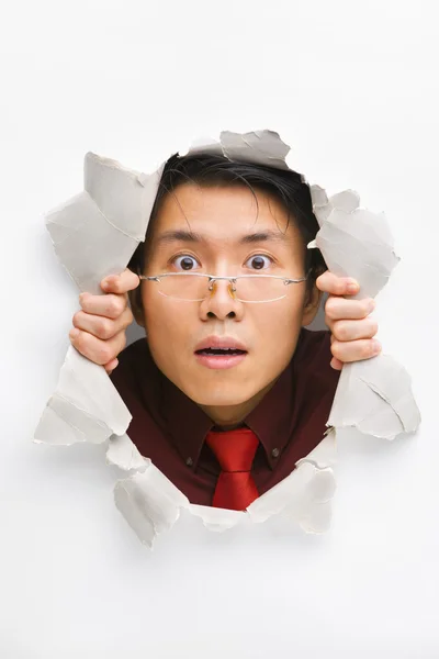 Man with funny expression gazing from hole in wall — Stockfoto