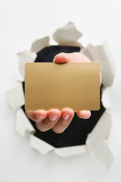 Mão breakthrough parede segurando vazio cartão dourado — Fotografia de Stock