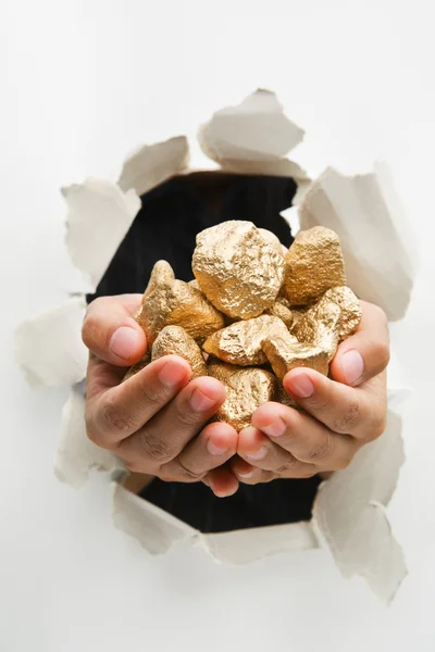 Hand breakthrough wall holding lumps of golden nuggets — Stock Photo, Image