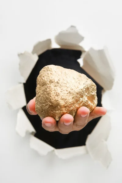 Hand breakthrough wall holding big lump of golden nugget — Stock Photo, Image