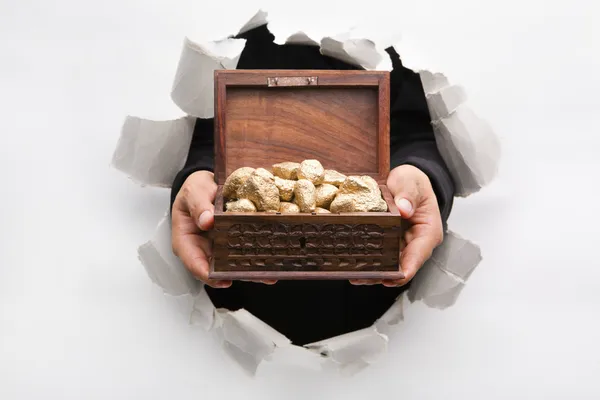 Hand breakthrough wall holding treasure chest full of golden nug — Stock Photo, Image