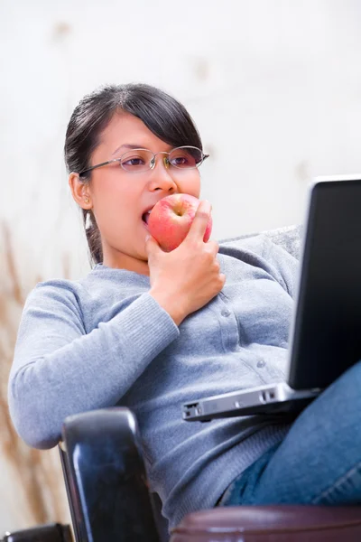 Junge Frau isst Apfel während sie auf ihren Laptop schaut — Stockfoto