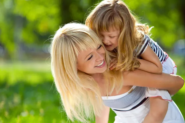 Schöne junge Mutter hält ihre kleine glückliche Tochter auf dem Rücken Stockbild