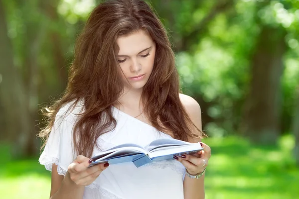 美丽的小女孩在公园里看书 免版税图库图片