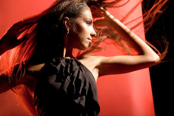 Portrait of gorgeous female wearing black evening dress dancing on red background