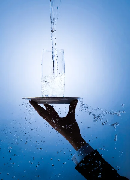 Imagem de garçons mão segurando bandeja com vidro sobre ele sendo derramado com água pura — Fotografia de Stock
