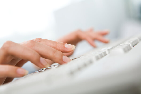 Close-up of female hand touching buttons of white computer keyboard