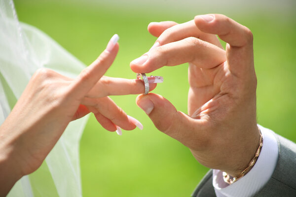 Grooms hand putting wedding ring on brides finger