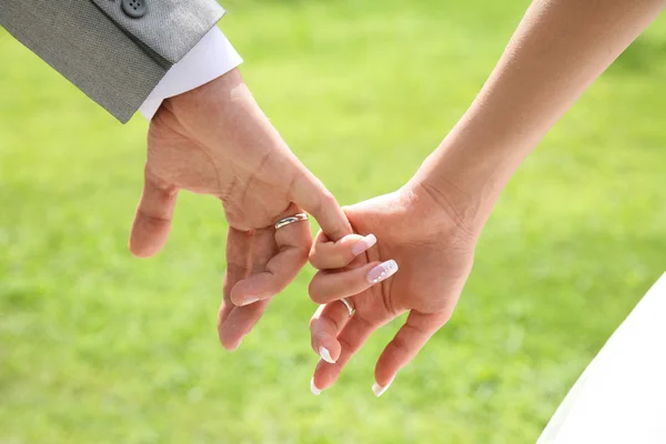 Primer plano de las novias mano sosteniendo la de su marido sobre fondo verde — Foto de Stock