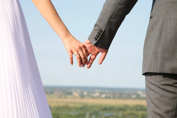 Жених и невеста держат друг друга за руки где-то снаружи — стоковое фото