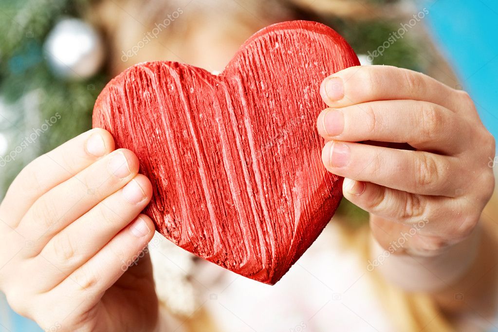 Close-up of red wooden heart in child's hands showing it