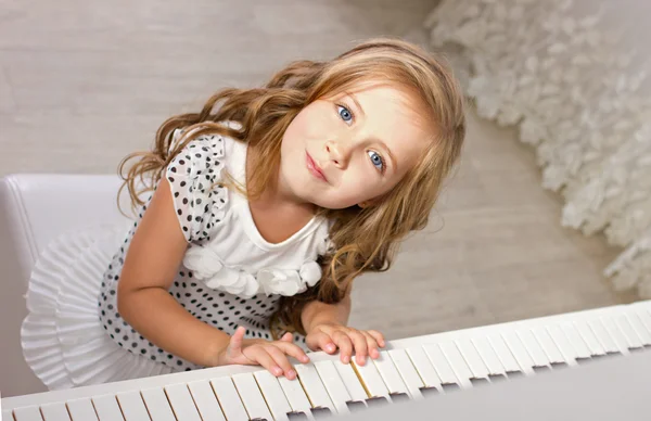 Hermosa niña rubia en bellezas sentada cerca de un piano — Foto de Stock