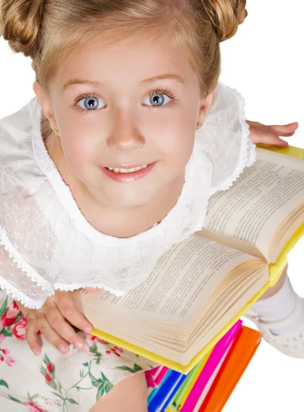 Schoolmeisje met boek zittend op hoop boeken — Stockfoto