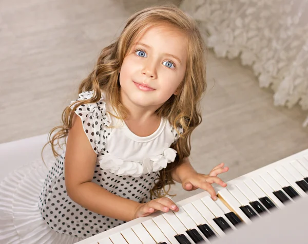 Маленькая девочка сидит рядом с пианино — стоковое фото
